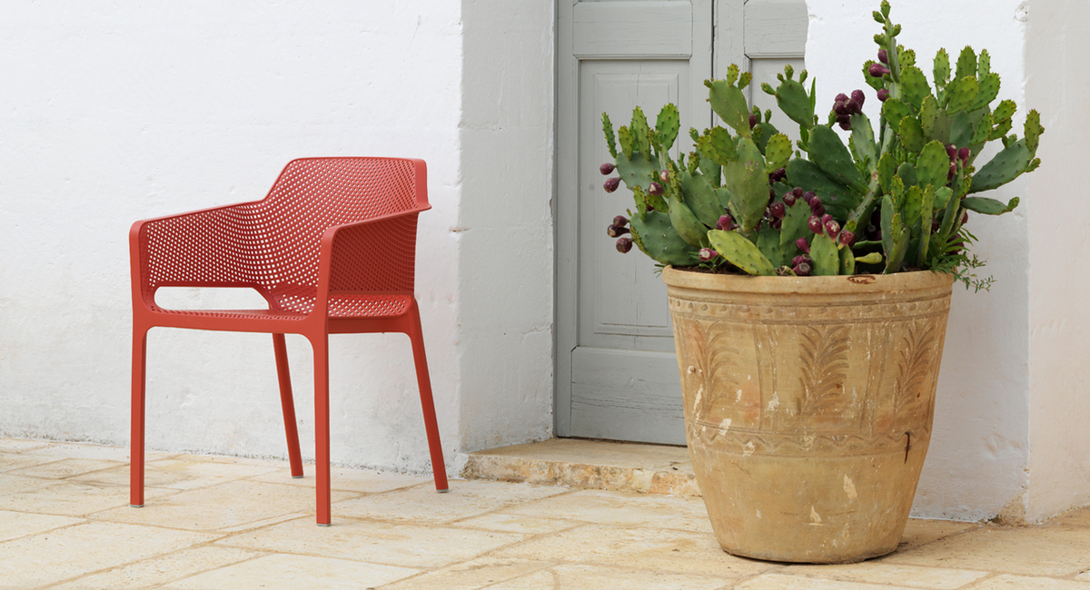 Nard net chair in coral red with pot plant next to mediterranean door
